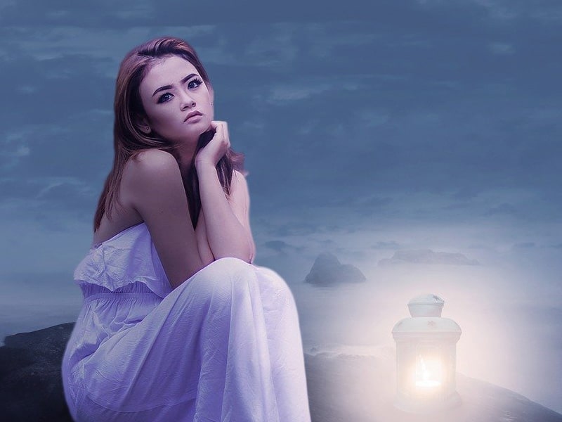 Pensive woman sitting on rocks near a lantern to illustrate the problem of how to get in the mood after a hysterectomy
