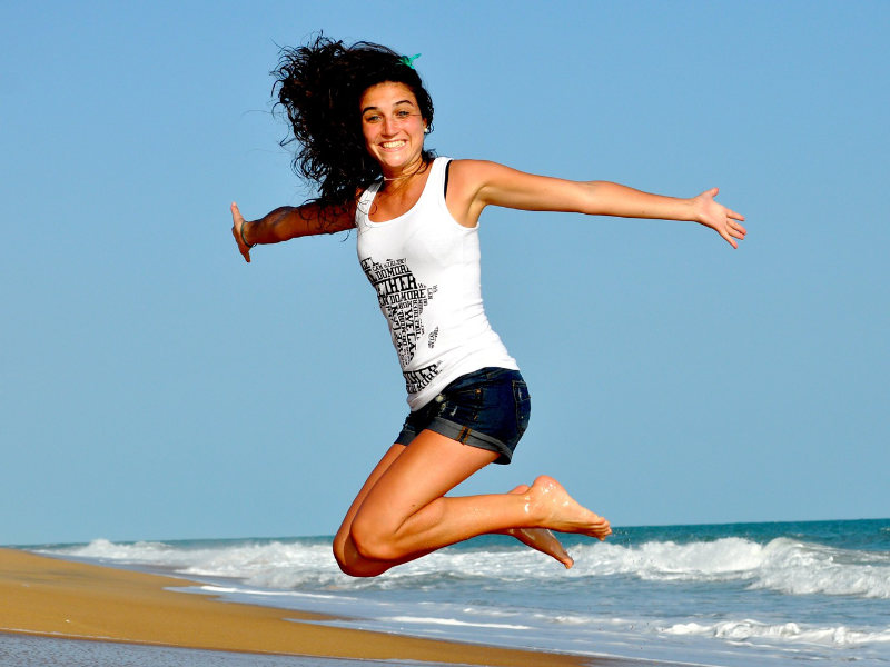 Slim and happy woman jumping on beach to illustrate Emsculpting