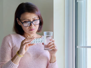 middle-aged woman trying to treat menopausal symptoms with pills and water