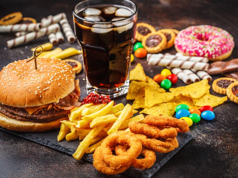 picture of unhealthy foods and a soda, including a cheeseburger, french fries, onion rings, tortilla chips, candy and donuts