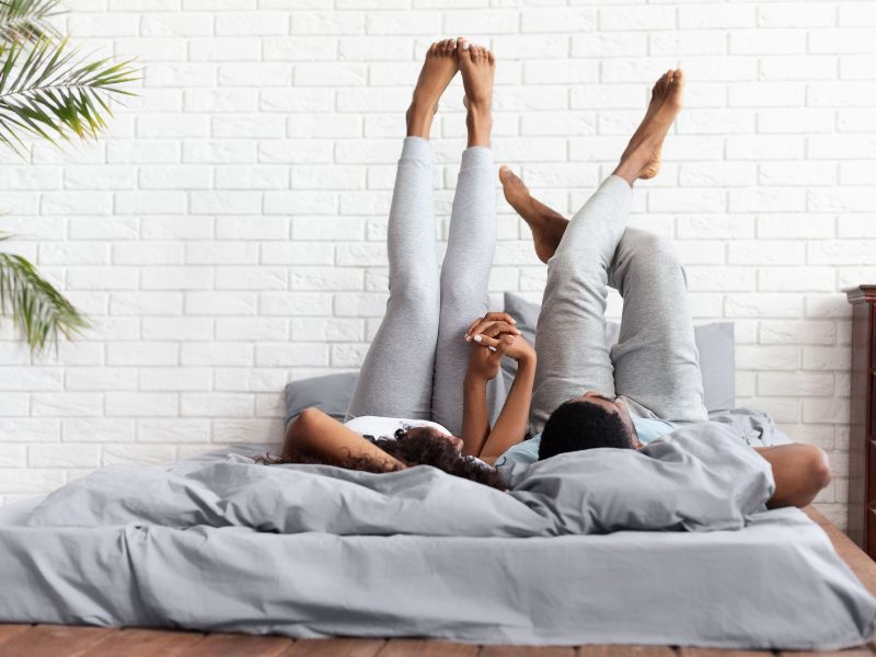 Happy couple lying on bed at home raising legs up
