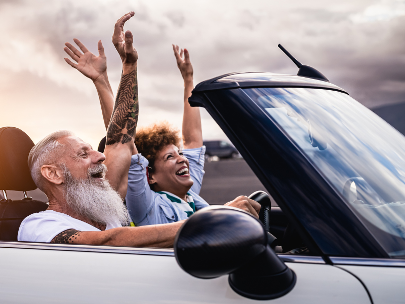 Older mixed raced couple throw their hands in the air in a convertable car