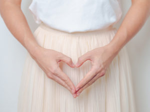 woman with heart-shaped hands framing her womb area