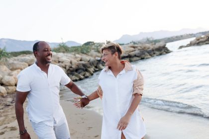 Middle ages couple walk hand in hand on a beach wearing white clothes