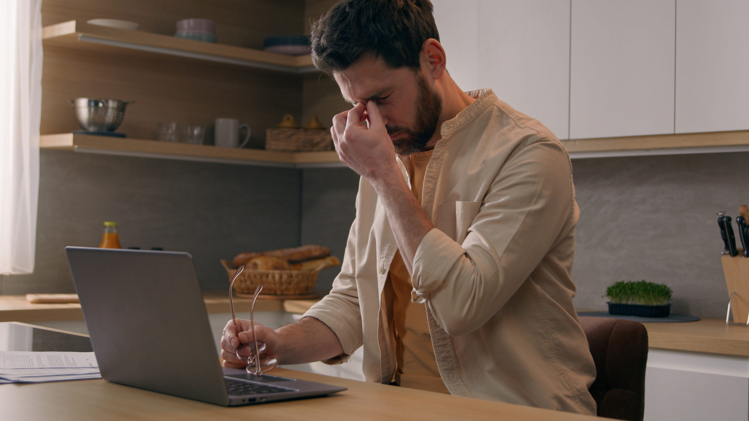 Caucasian man working laptop at kitchen suffer with eyestrain take of glasses. Tired male freelancer businessman work with computer at home feel eyes pain discomfort with eyeglasses exhausted eyesight