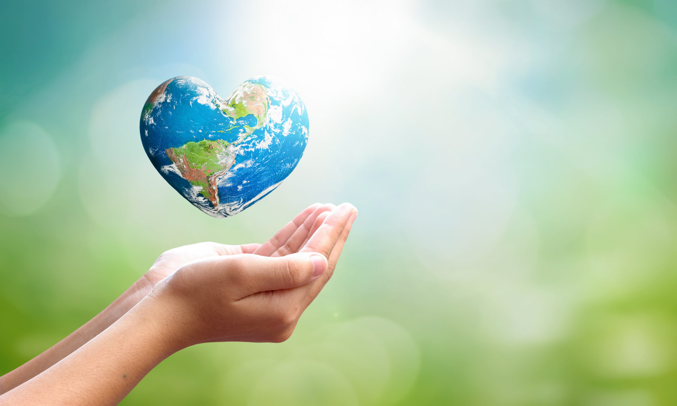 World environment day concept: man opens palms and drags heart shaped earth globe over blurred blue sky and water background. Elements of this image furnished by NASA. To illustrate root-cause healthcare