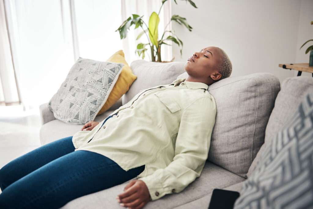 Tired, sleep and black woman on a home sofa for relax, stress relief or lazy after work. Mental health, living room and an African girl on a couch for rest, sleep or burnout with insomnia or fatigue and poor sleep due to menopause