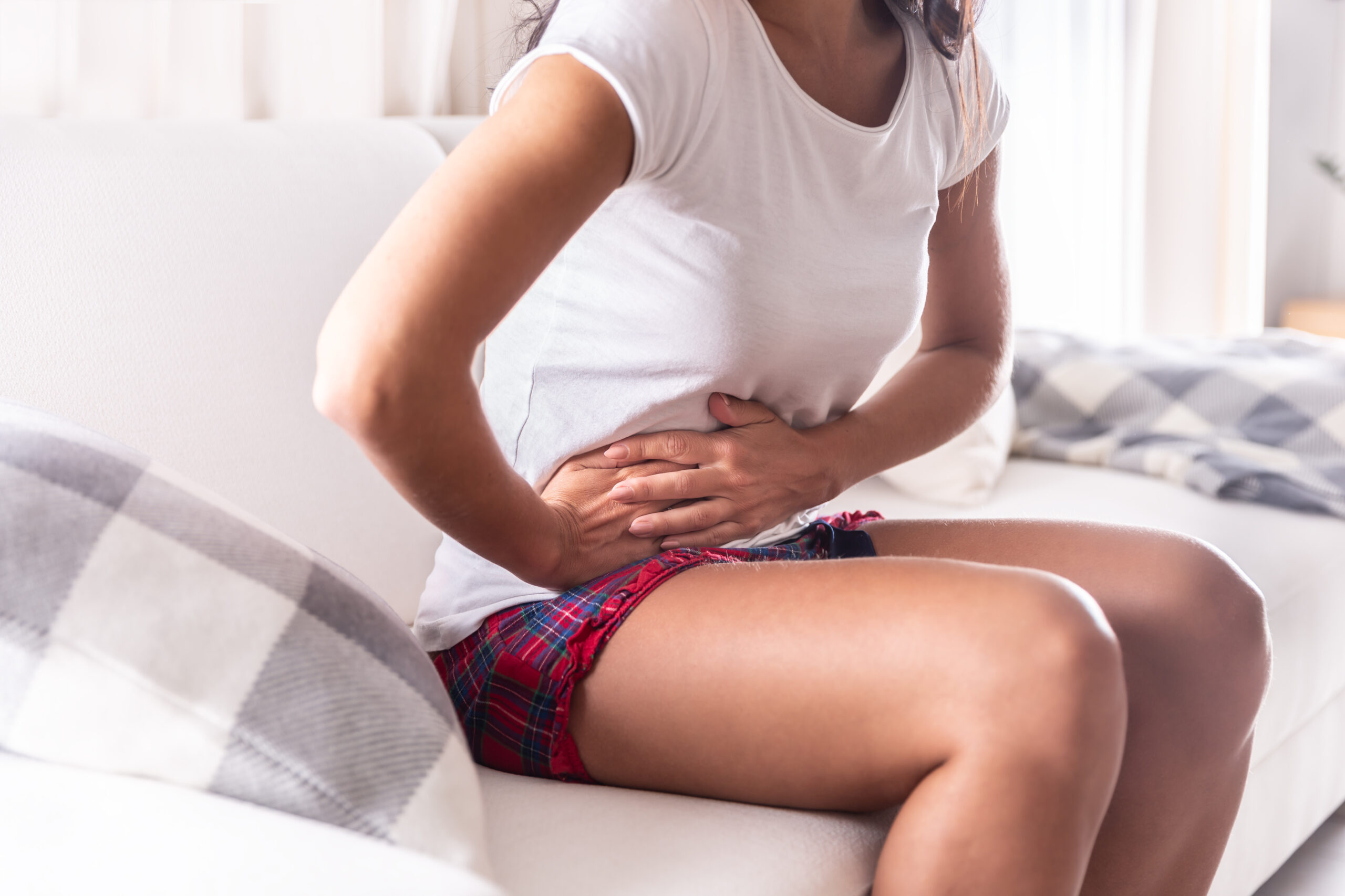 Woman sitting on a couch at home holding her stomach in distress