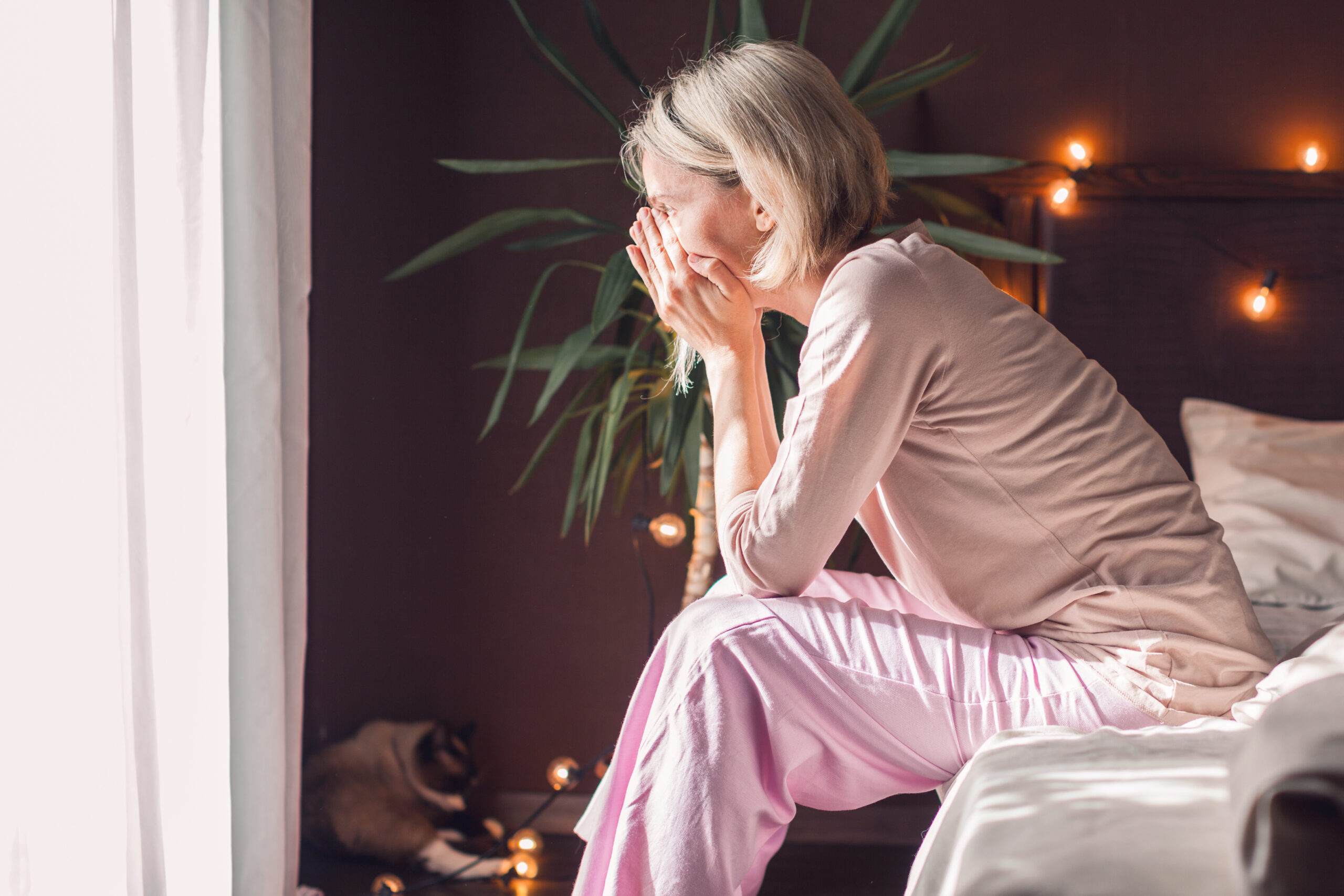 Unhappy sad middle aged woman sitting on bed at home