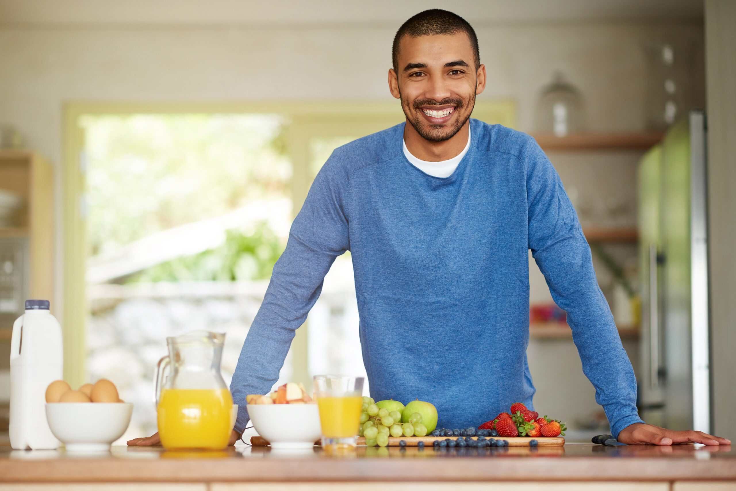 Man, portrait and healthy fruit for breakfast nutrition or meal prep as gut health, wellness or antioxidants. Male person, face and smile at kitchen counter with orange juice or organic, eggs or home