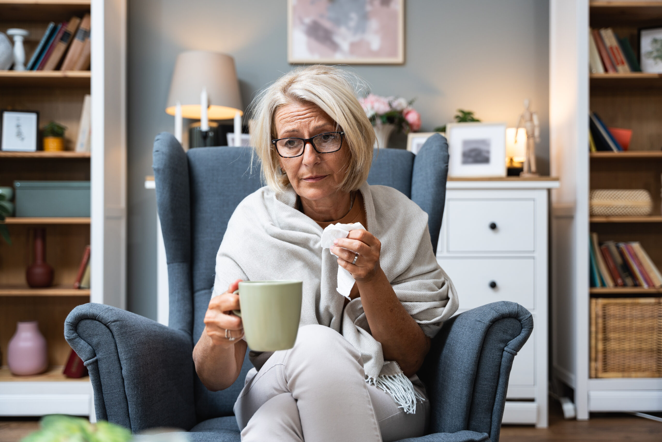 Senior woman sick and blowing nose at home from virus, allergy and illness on couch. Tired, tissue and elderly female person in a house lounge with sneeze from cold and flu on a sofa with allergies