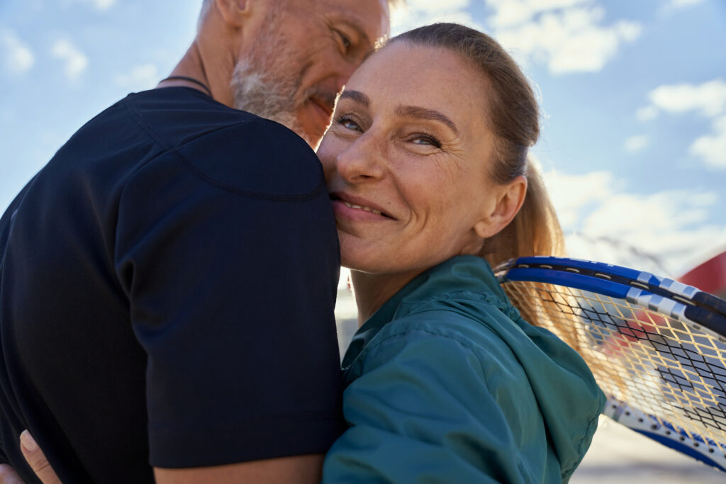 Portrait of active mature couple looking happy while embracing each other outdoors, ready for morning workout on tennis court