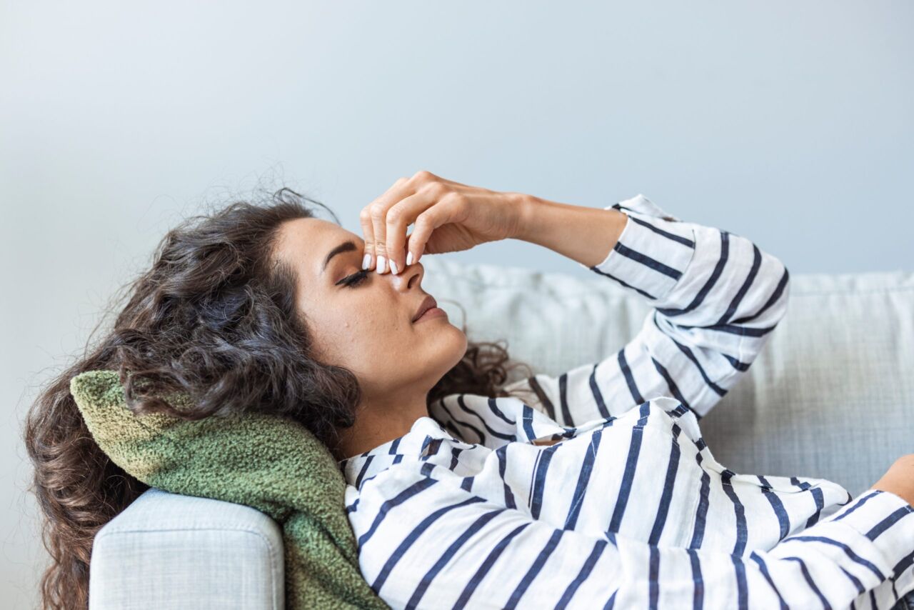 Upset depressed young woman lying on couch feeling strong headache migraine, sad tired drowsy exhausted girl resting trying to sleep after nervous tension and stress, somnolence concept